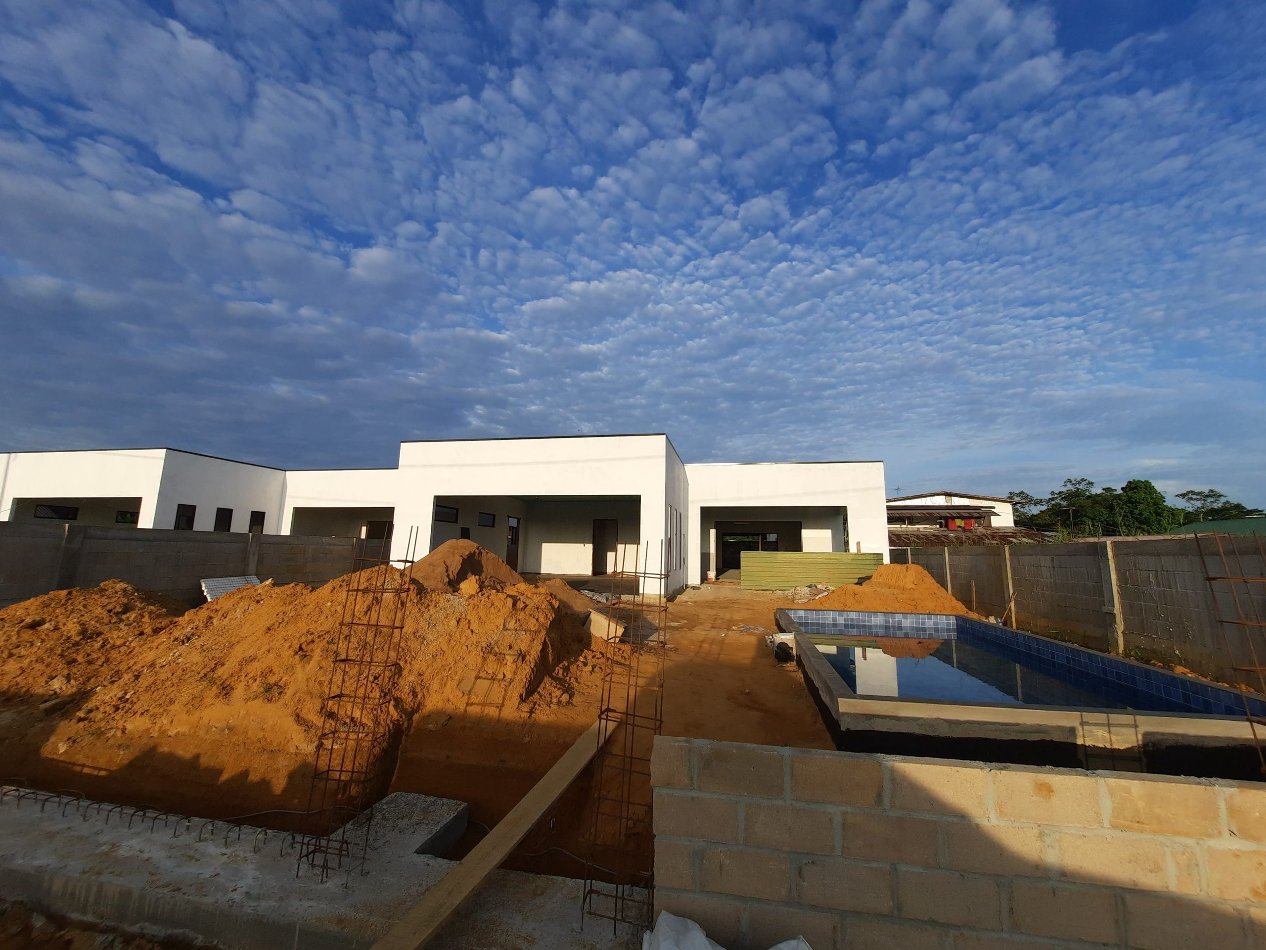 Bouwproject van Basiton Group. Enkele luxe huizen in aanbouw met hopen zand en een onafgemaakt zwembad aan de voorkant.